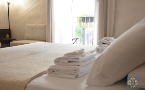 Un lit bien fait, avec des serviettes pliées, une table de chevet avec une lampe, et une vue sur la verdure à l’extérieur.