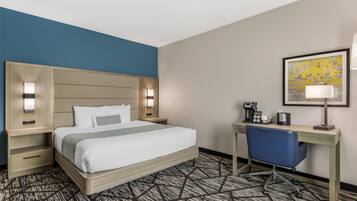 Quarto de hotel com cama, escrivaninha, cadeira e um quadro na parede.