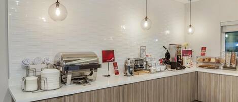 A modern kitchen area with a white countertop, stainless steel appliances, and hanging pendant lights.