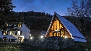 A cozy A-frame cabin with a stone foundation, large windows, and a well-lit interior. - Hôtel Ô Chiroulet (Bagnères-de-Bigorre)