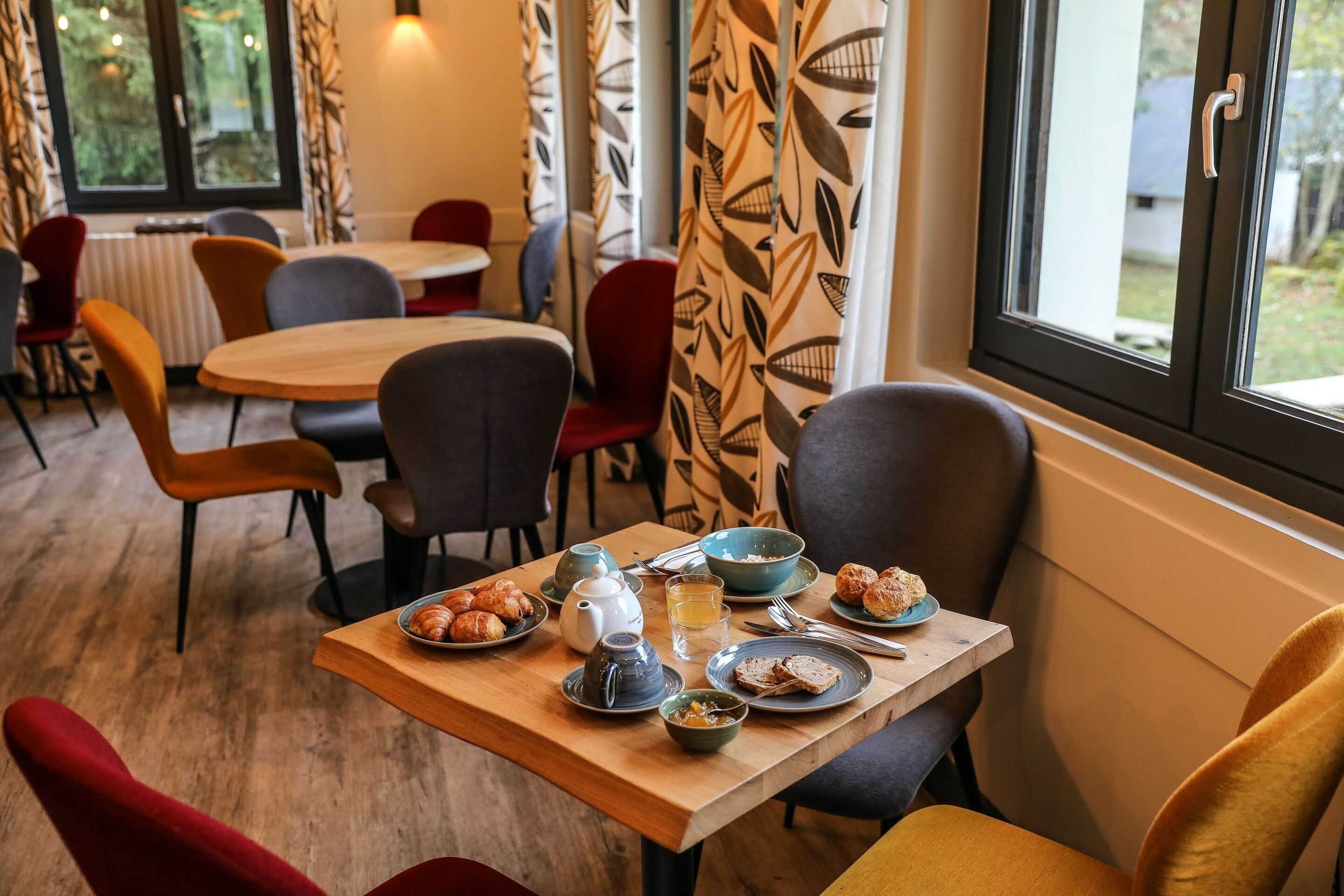 A cozy dining area with wooden tables and chairs, a variety of dishes, and a view of the outdoors through large windows.