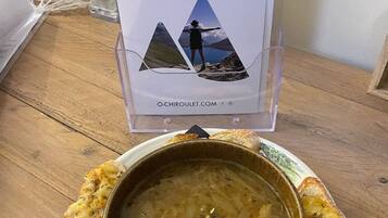 A wooden table with a bowl of soup and toasted bread, a sign with 'CHIROULET MONTAGNE DE VIE' and a website URL, and a decorative string of lights in the background.
