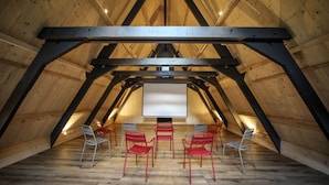 An attic room with a sloped wooden ceiling, a projector screen, and several chairs arranged for viewing. - Hôtel Ô Chiroulet (Bagnères-de-Bigorre)