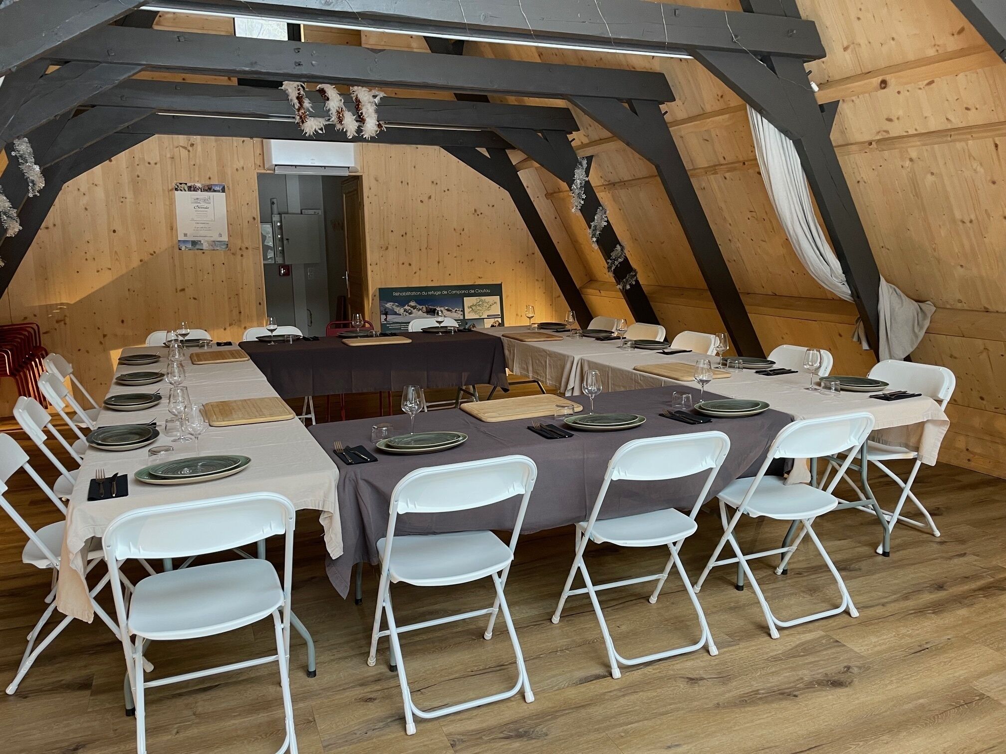 A dining area with tables set for six, white folding chairs, and a wooden ceiling structure.