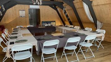 A dining area with tables set for six, white folding chairs, and a wooden ceiling structure.