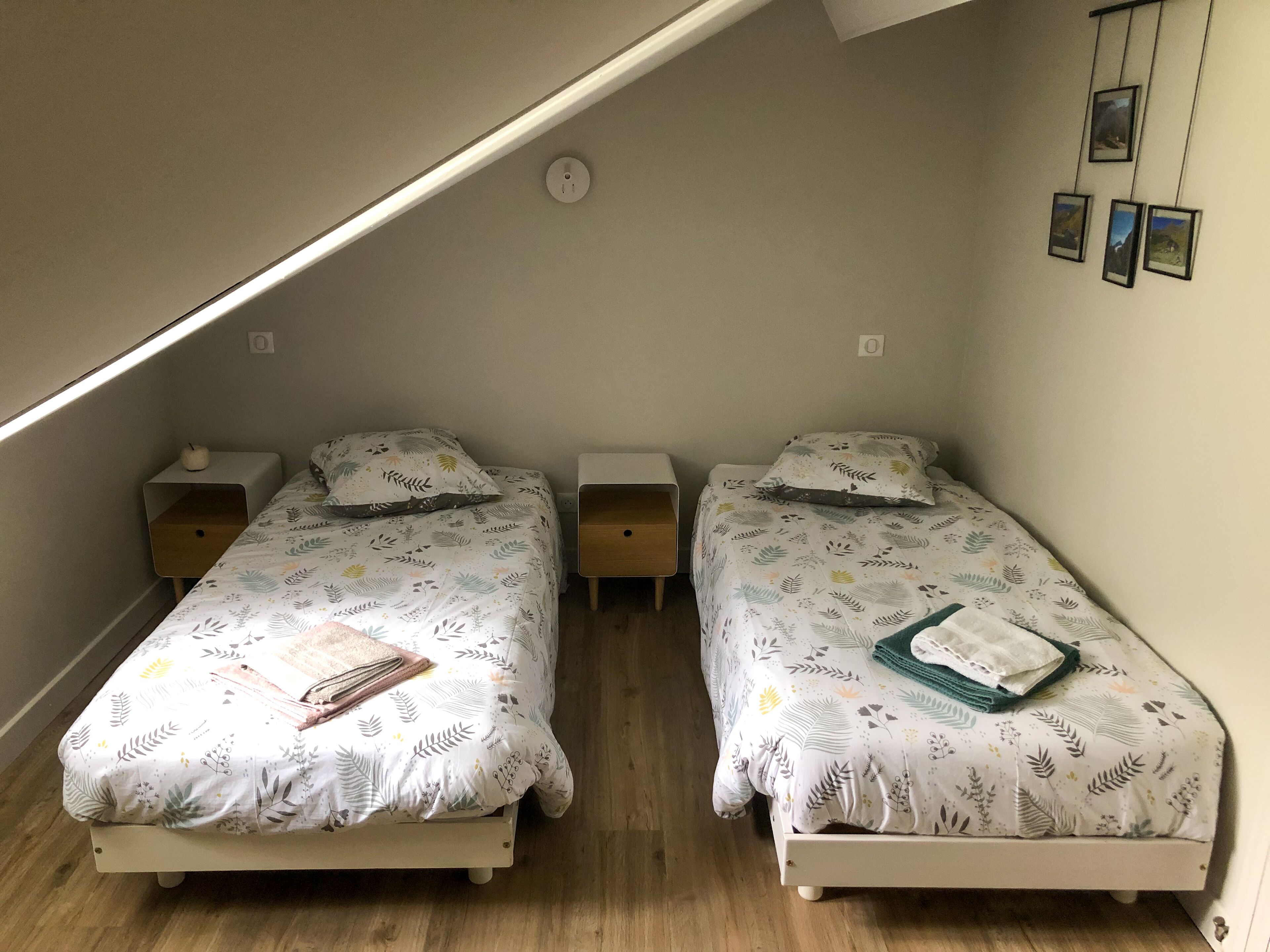 Une petite chambre agréable, dotée de deux lits simples, chacun avec une table de chevet. La chambre a un plafond en pente et une petite fenêtre.