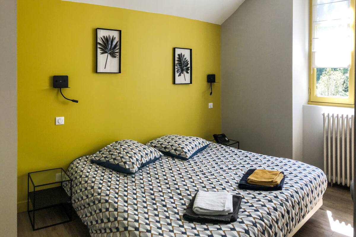 A room with a bed, a telephone, and a window with a view of trees.