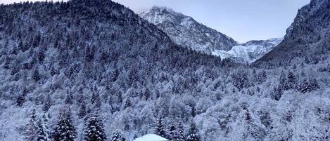 Un edificio blanco con techo inclinado, rodeado de árboles y montañas cubiertas de nieve.