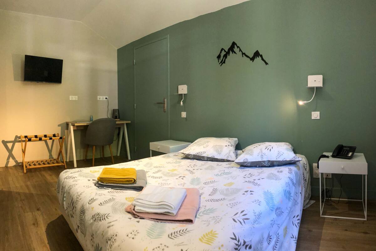 A bedroom with a bed, a desk, a chair, a TV, and a phone.