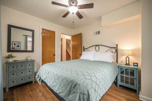 A bedroom with a bed, dresser, nightstand, ceiling fan, and a door leading to another room.
