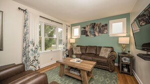A living room with a brown leather sofa, a wooden coffee table, and a green patterned rug. - Sweet Escape Near Historic Main St, 4BR, 2 Baths (Saint Charles)