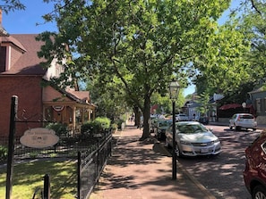 A street view with parked cars, a brick building labeled 'The Homestead,' and a sidewalk lined with trees.