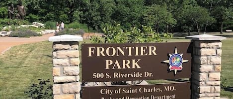 Placa indicativa para o Frontier Park, com um pilar de pedra, céu claro e vegetação ao fundo.