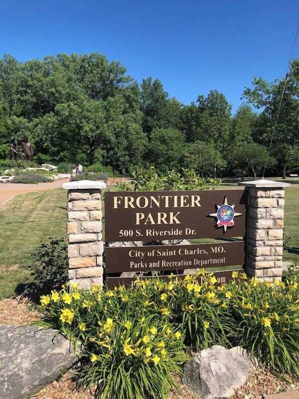 A sign for Frontier Park with a stone pillar, a clear sky, and greenery in the background.