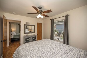 Une chambre à coucher avec un lit, un ventilateur de plafond, un miroir et une fenêtre avec des rideaux.