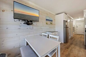 Una cocina con pared de madera, un televisor de pantalla plana montado sobre una mesa y un refrigerador.