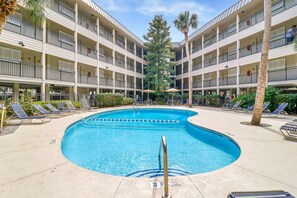 A pool area with lounge chairs and a building with multiple balconies.