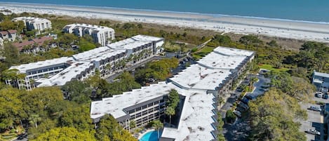 Un complexe hôtelier situé sur la côte, composé de plusieurs bâtiments, doté d’aires de stationnement et offrant une vue sur la plage.