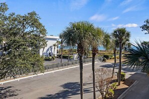 A parking lot with a building in the background, surrounded by palm trees and a clear sky.