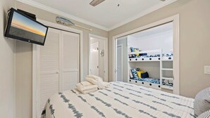 Ein Schlafzimmer mit einem Bett, einem an der Wand montierten Fernseher, einem Kleiderschrank und einem eingebauten Schlafplatz mit Stauraum.