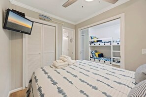 A bedroom with a bed, a TV mounted on the wall, a wardrobe, and a built-in bunk bed with storage.