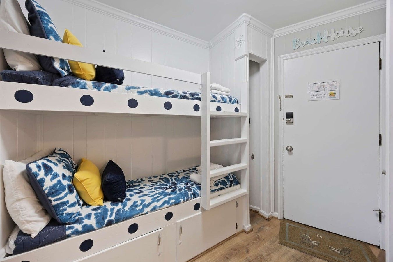 Une chambre avec des lits superposés, une porte portant l’inscription « Maison d’hôtes » et une carte accrochée au mur.