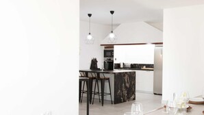 A modern kitchen with a central island, bar stools, and a dining area set for six with round white plates and wine glasses. - Villa with Private Pool (Alberique)