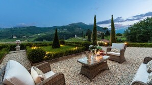 An outdoor seating area with wicker furniture and a table set for dining, overlooking a scenic landscape with hills and trees. - VILLA REGINA, 4 bedrooms and a luxury style among the vineyards by Lucca Town (Lucca)