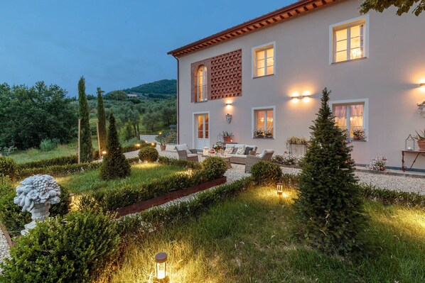 A two-story house with a garden patio, outdoor seating, and decorative lighting.