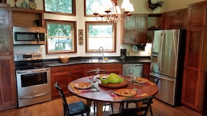 Una cocina con armarios de madera, electrodomésticos de acero inoxidable, una mesa de comedor para cuatro personas y ventanas amplias.