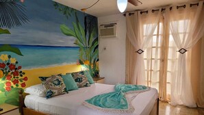 A bedroom with a bed, a nightstand, a ceiling fan, and a mural of a beach scene. - Costa del Sol Pousada (Búzios)