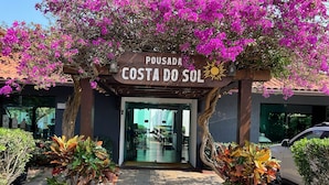 A hotel entrance with a sign reading "Pousada Costa do Sol," surrounded by potted plants and a car parked nearby. - Costa del Sol Pousada (Búzios)
