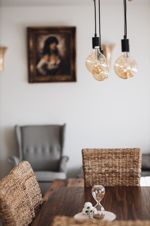 A dining area with wicker chairs, a wooden table, and hanging light fixtures.
