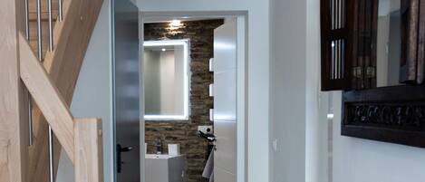 A hallway with a wooden staircase, a stone wall, and a modern bathroom with a mirror and sink.