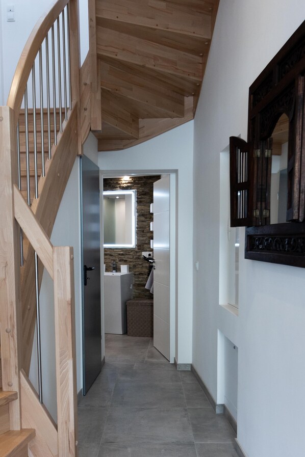 A hallway with a wooden staircase, a stone wall, and a modern bathroom with a mirror and sink.