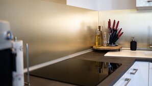 A modern kitchen with a black induction cooktop, a wooden cutting board with kitchen utensils, and a white countertop. - Vacation with a view of the unique Marksburg Castle (Braubach)