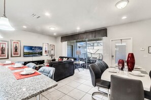 A modern kitchen with granite countertops, a dining area with a table set for four, and a living area with a sofa and TV.