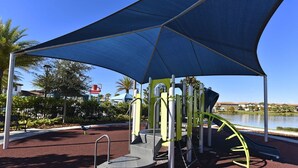 A playground with a blue canopy, a slide, and a climbing structure.