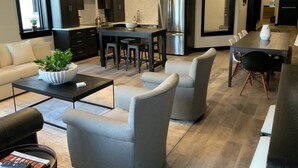 A modern kitchen with dark cabinets, a stainless steel refrigerator, and a dining area with a table and chairs. - Cassius Quarters@The713! Downtown, large, upscale suite w/private balcony (Louisville)