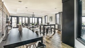 A modern dining area with a long table, chairs, and a kitchen area with a refrigerator and cabinets. - Cassius Quarters@The713! Downtown, large, upscale suite w/private balcony (Louisville)