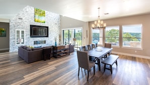 A spacious living area with a stone accent wall, a large flat-screen TV, a dining table with chairs, and a fireplace.