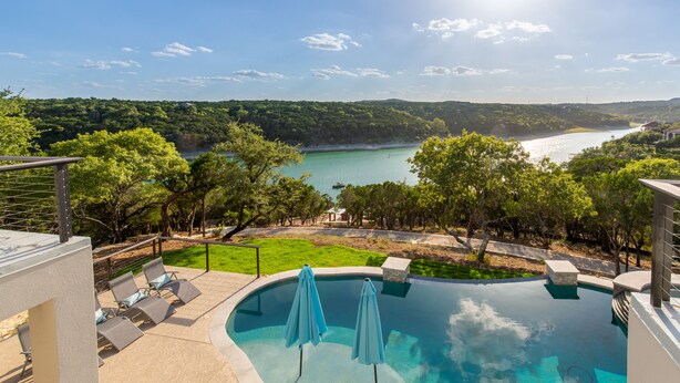 A swimming pool with lounge chairs and umbrellas, surrounded by greenery and a view of a lake.