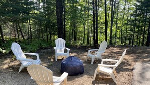 Ein Campingplatz mit vier weißen Adirondack-Stühlen, die kreisförmig um einen blauen Sitzsack angeordnet sind.