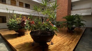 Een ruime atrium met meerdere verdiepingen, een houten tafel in het midden met potplanten, en een glazen plafond dat natuurlijk licht doorlaat.