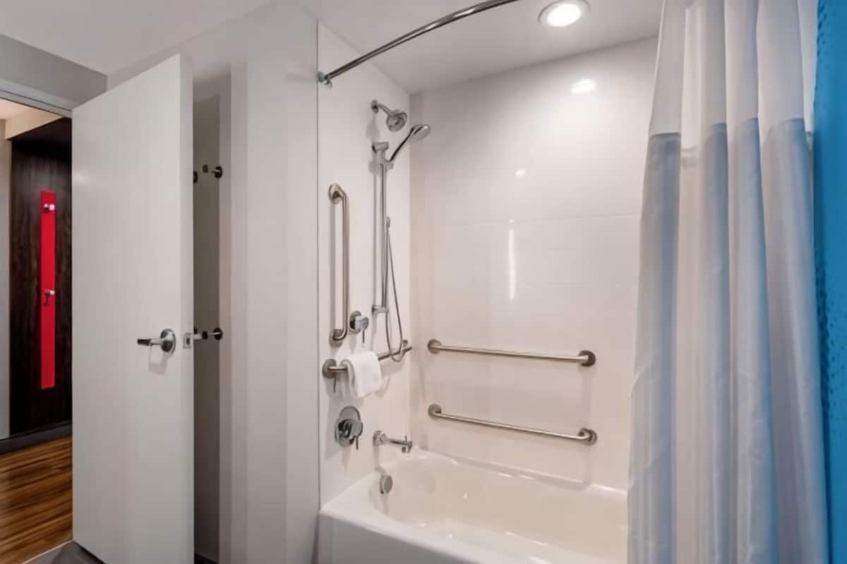 Un baño moderno con ducha a ras de suelo, barras de apoyo y bañera.