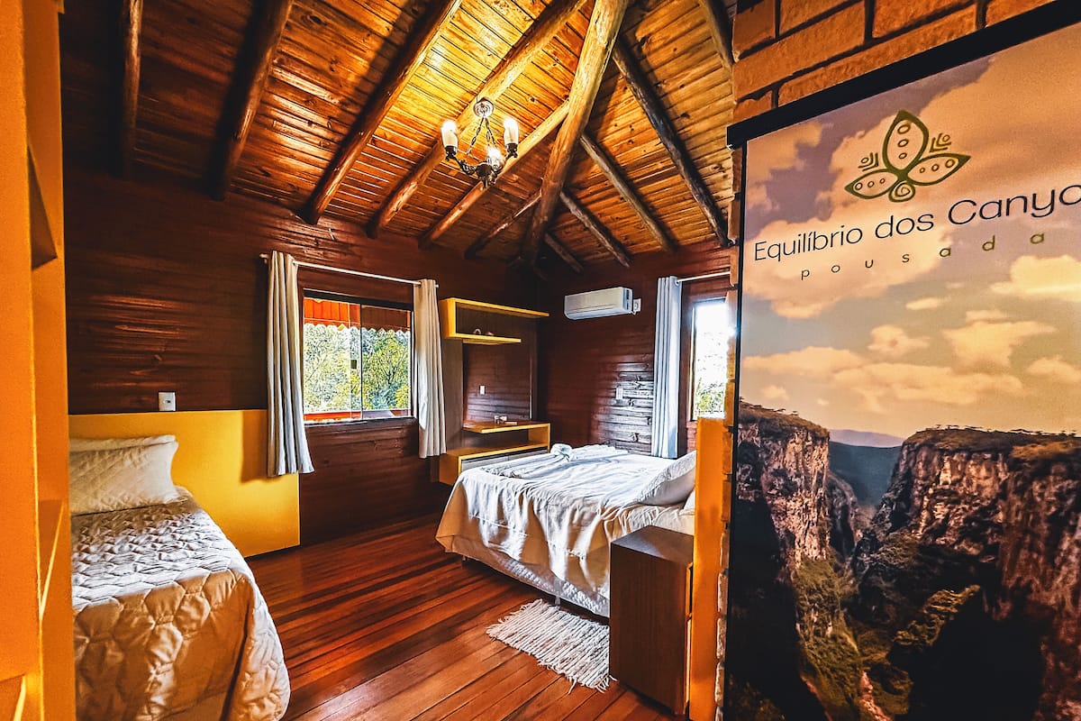 Quarto de madeira com duas camas, uma janela e ar-condicionado fixado na parede.