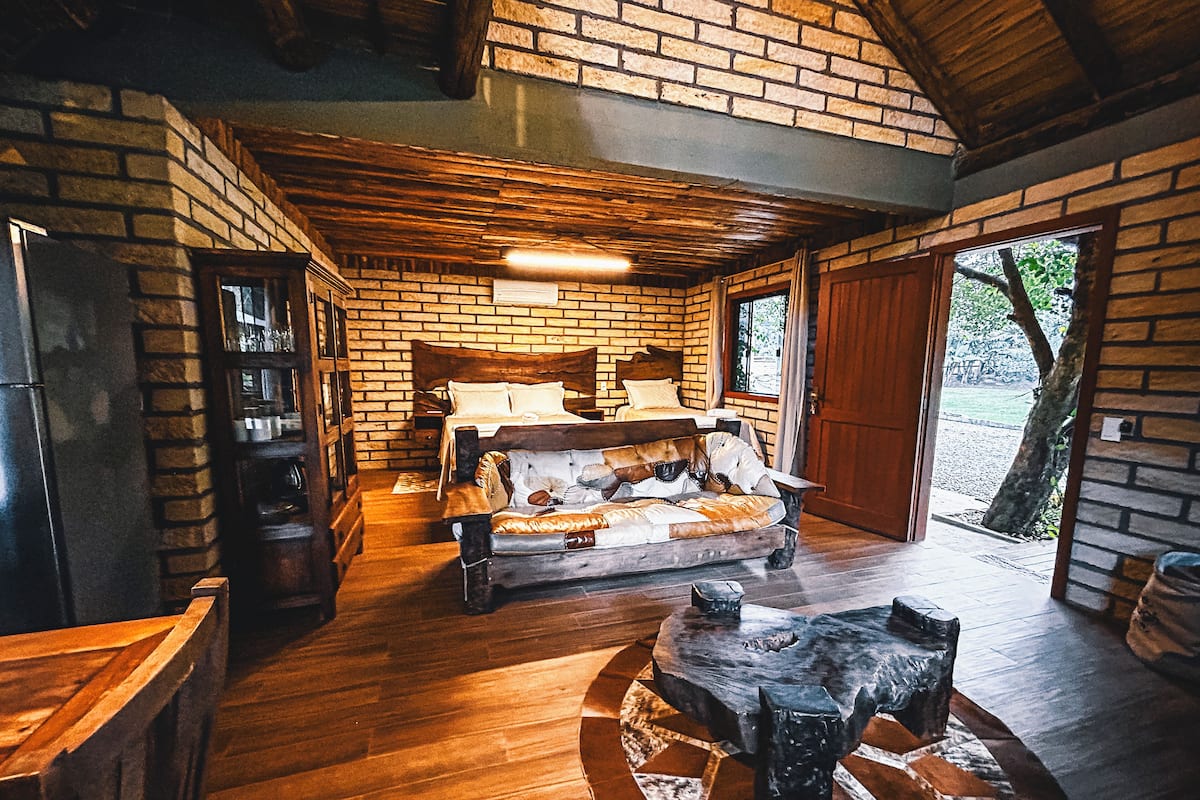 Um quarto rústico com uma cama de madeira, uma lareira de pedra e uma janela grande.