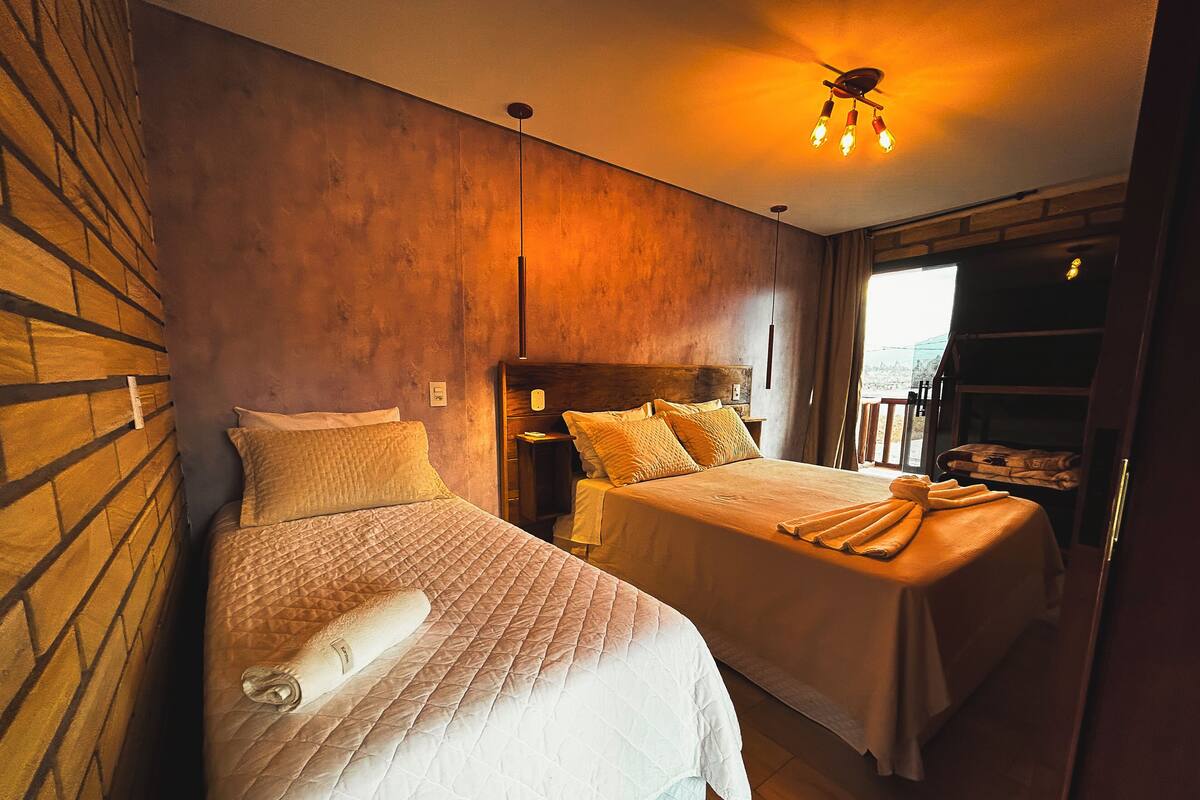 Quarto de hotel com duas camas, parede de madeira, luminária no teto e janela com vista.