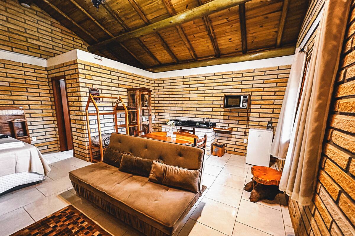 Um quarto aconchegante com parede de tijolos, teto de madeira, sofá, cama e televisão.