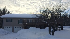 Una casa de dos pisos con un porche cubierto y un garaje. Nieve acumulada frente a la casa.